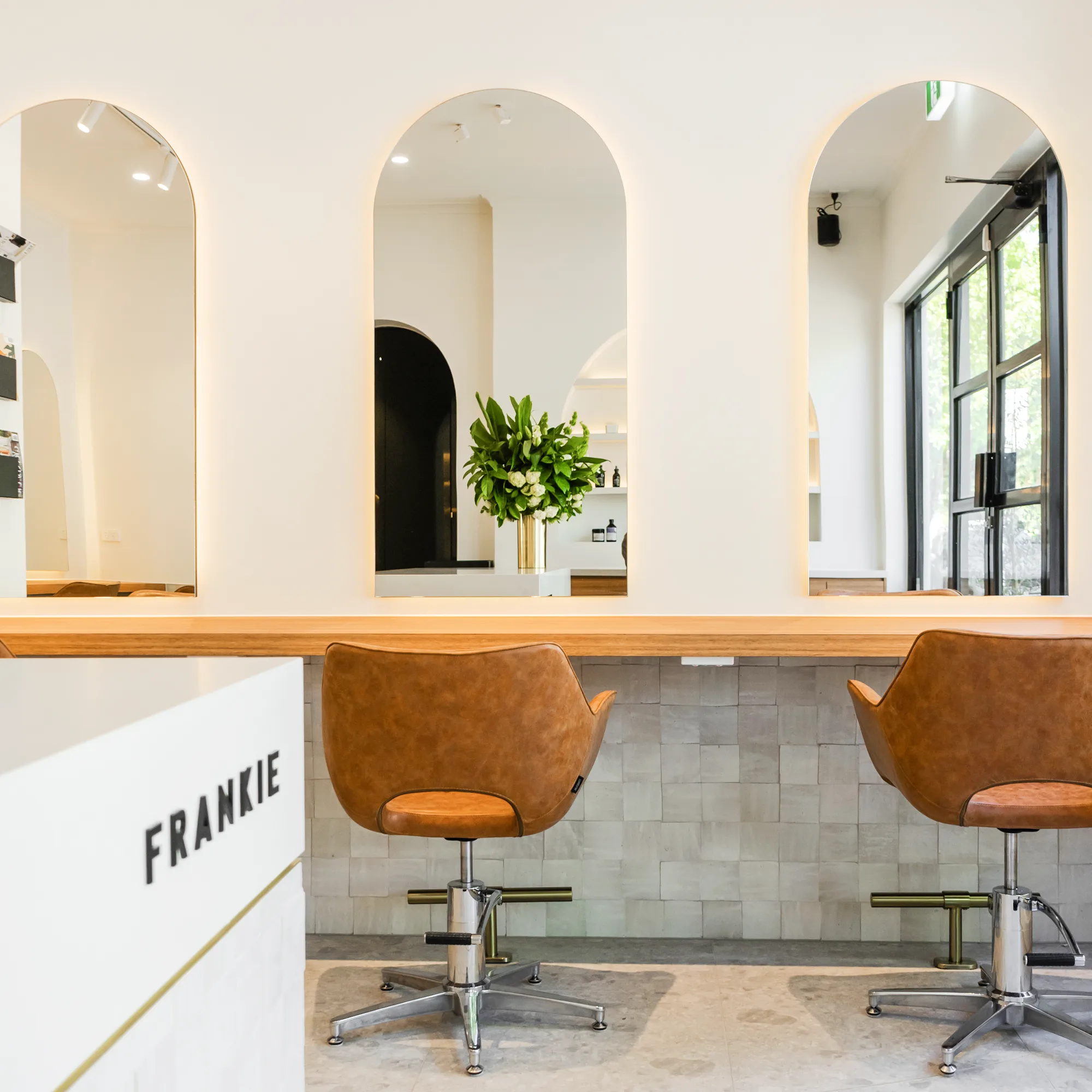 Frankie's signature arched niche mirrors with tan leather styling chairs and zellige tiles